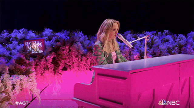 a woman is singing into a pink microphone while playing a pink piano
