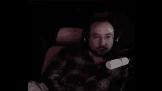 a man wearing headphones and glasses is sitting in a car with a microphone in his hand .