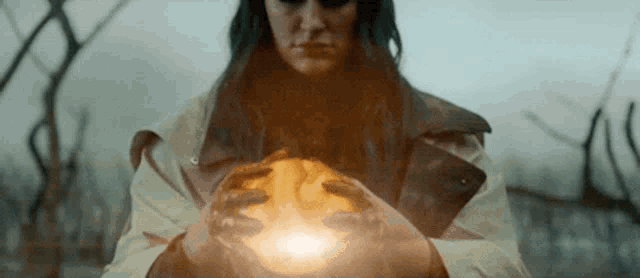 a woman in a trench coat holds a glowing object in her hands