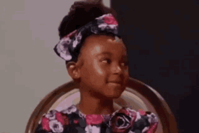 a little girl is sitting in a chair wearing a headband and a floral dress .