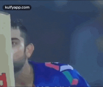 a man in a blue shirt is holding a cricket bat behind his face .