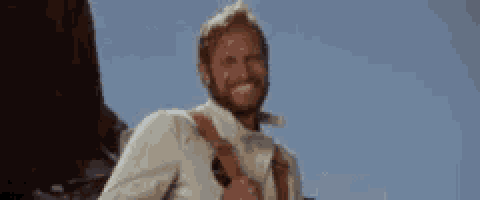 a man with a beard is smiling while holding a gun in his hand .