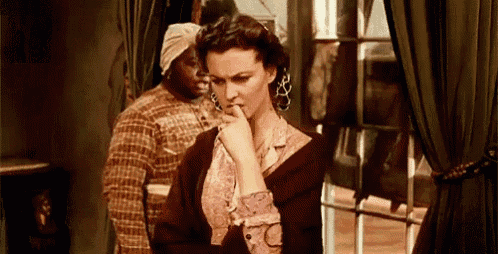 a woman is standing in front of a window with her hand on her chin and a man is standing behind her .
