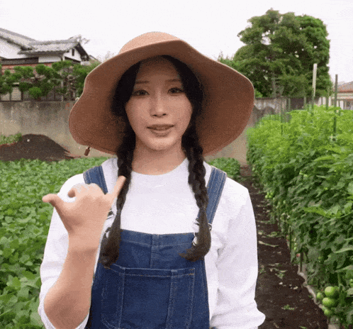 a woman wearing overalls and a hat stands in a field