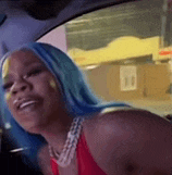 a woman with blue hair is sitting in the driver 's seat of a car and smiling .