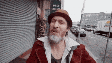 a man with a beard is standing in front of a deli grocery store