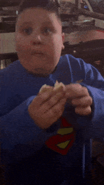 a young boy wearing a blue superman sweatshirt is eating something