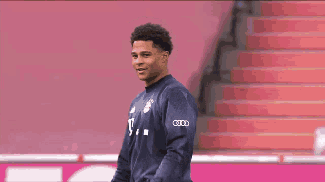 a young man wearing an audi sweatshirt stands in front of a pink staircase