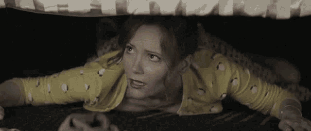 a woman in a yellow sweater is hiding under a blanket .