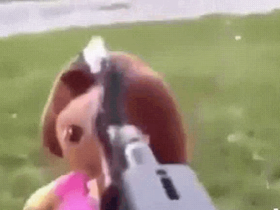 a barbie doll is holding a gun in front of her face .