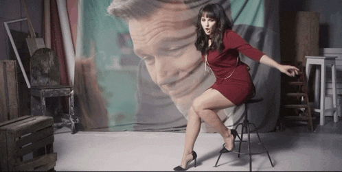 a woman in a red dress is sitting on a stool in front of a painting