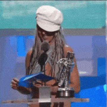 a woman wearing a white hat is standing in front of a microphone holding a trophy