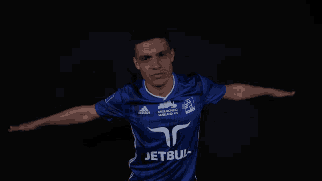 a man with his arms outstretched wears a blue adidas jersey