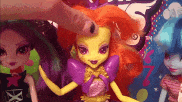 a doll with orange hair and a purple dress has a tm sticker on it
