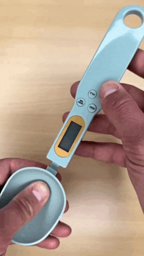 a person is holding a digital measuring spoon with a display that says grams