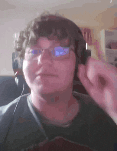 a man wearing glasses and headphones holds his hand to his ear