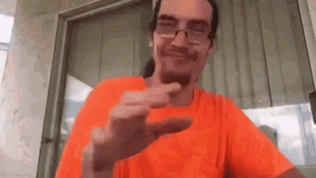 a man wearing glasses and an orange shirt is making a funny face .