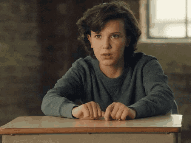 a young woman is sitting at a desk with her hands on the desk