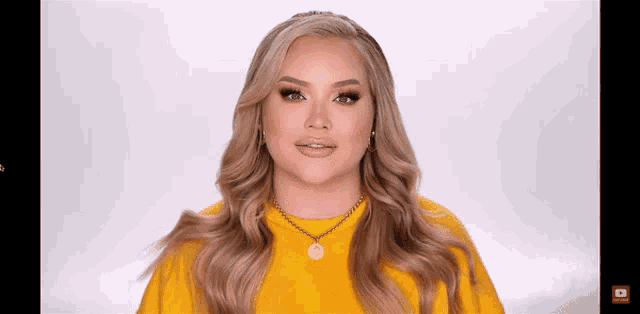 a woman wearing a yellow sweater and a gold necklace is looking at the camera