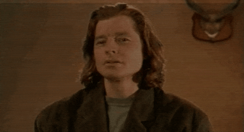 a man with long hair is standing in front of a wall with a deer head mounted on it .