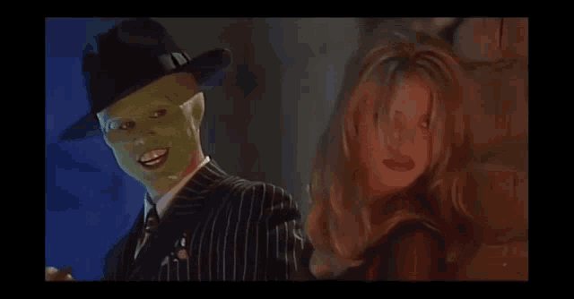 a man wearing a green mask is standing next to a woman in a red dress