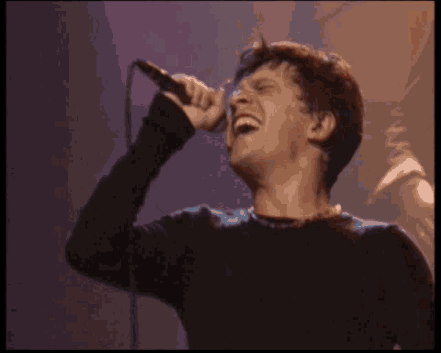 a man singing into a microphone in front of a crowd with their hands in the air