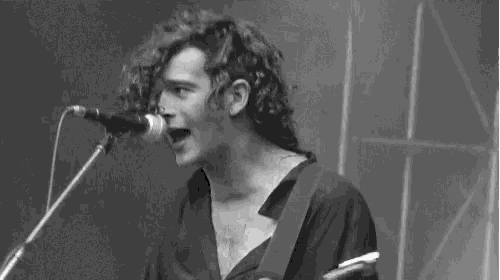 a black and white photo of a man singing into a microphone while holding a guitar