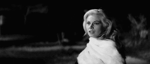 a woman in a fur coat is standing in a field at night in a black and white photo .
