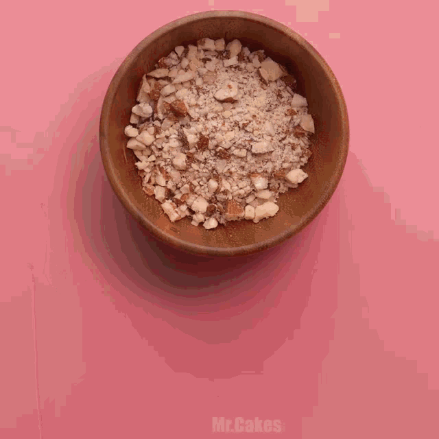 a wooden bowl filled with nuts on a pink surface