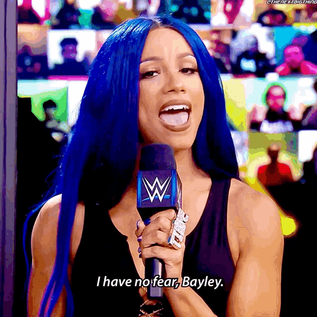 a woman with blue hair holds a microphone and says i have no fear bayley