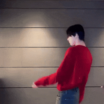a man wearing a red sweater is dancing in front of a wall