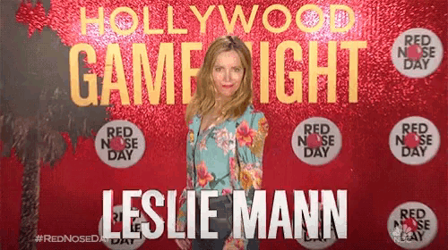 a woman stands in front of a hollywood game night backdrop