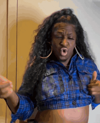 a woman in a blue plaid shirt is making a funny face and giving a thumbs up