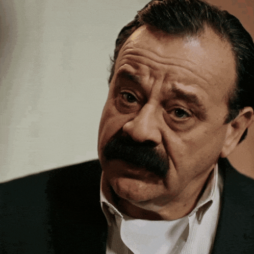 a man with a mustache is wearing a black suit and white striped shirt
