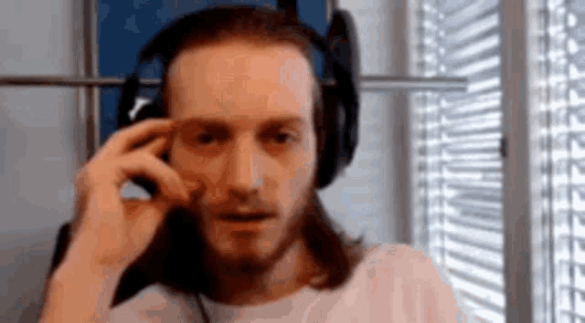 a man with long hair and a beard wearing headphones is sitting in front of a window .