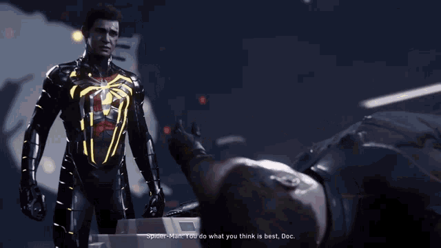 a man in a black suit with a yellow spider on his back is standing next to a man laying on the ground