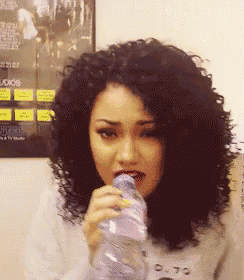 a woman with curly hair drinking from a bottle