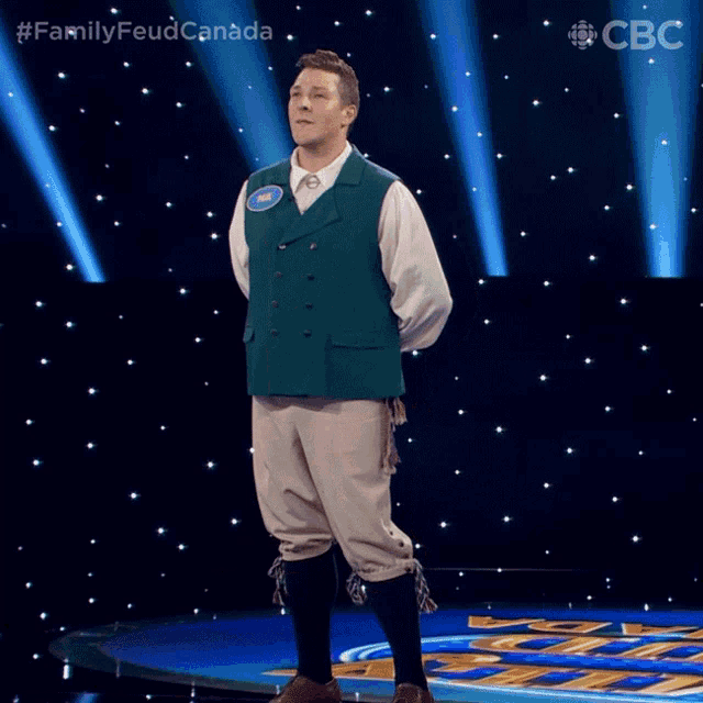 a man in a green vest and white shirt is standing on a stage with a cbs logo behind him