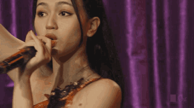 a close up of a woman singing into a microphone with the word one in the corner