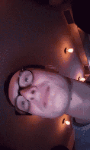 a man with glasses is making a face in a dark room