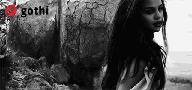 a black and white photo of a woman standing on top of a rock .
