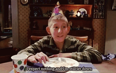 a young boy wearing a birthday hat is sitting at a table with a plate of food and a cup .