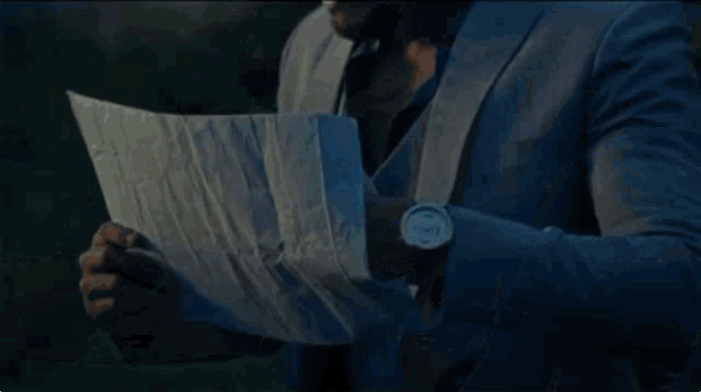 a man in a suit is holding a piece of paper and reading it .