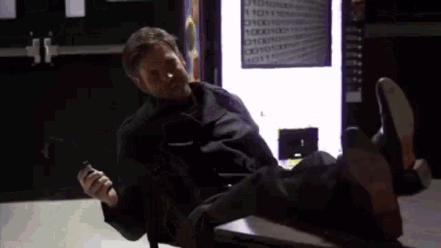 a man is sitting on a table with his feet up and holding a cell phone .