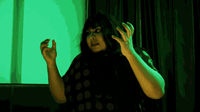 a woman in a black polka dot shirt is making a scary face in front of a green background