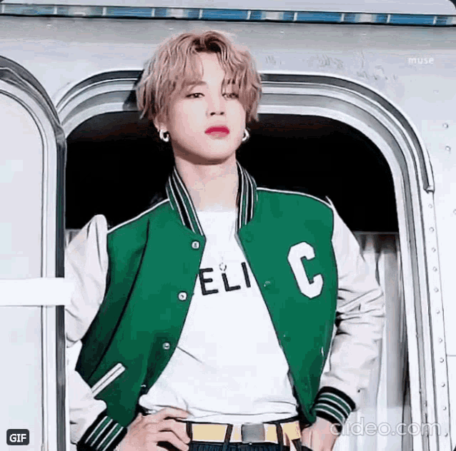 a young man wearing a green and white jacket and a white t-shirt is standing in front of a door .