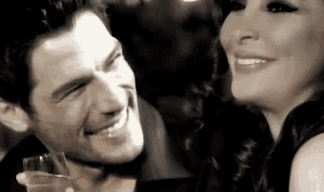 a man and a woman are smiling at each other while holding a glass of wine .