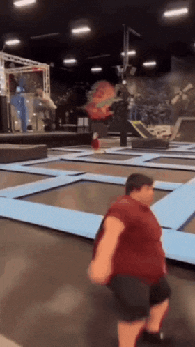 a fat man is jumping on a trampoline in a gym