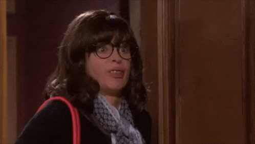 a woman wearing glasses and a scarf is making a funny face while standing in front of a door .