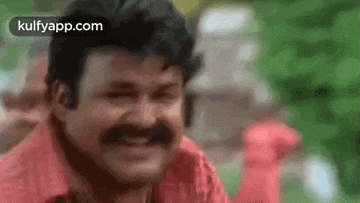 a man with a mustache and a red shirt is smiling and making a funny face .